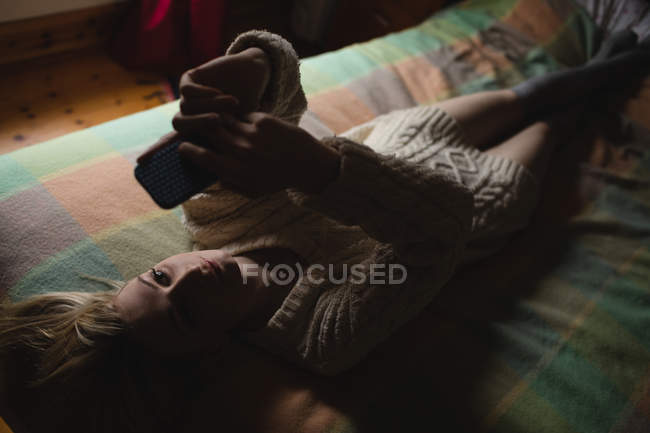 Женщина лежит и с помощью мобильного телефона на кровати в спальне — стоковое фото