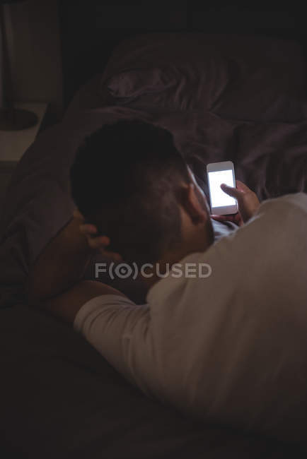 Uomo che usa il cellulare mentre si rilassa a letto a casa — Foto stock