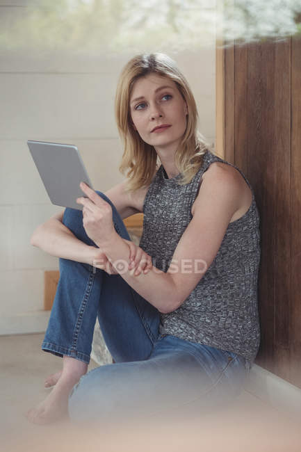Задумчивая женщина, использующая цифровой планшет дома — стоковое фото