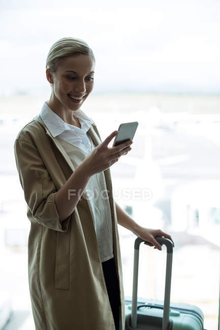 Businesswoman with luggage using mobile phone at airport — Stock Photo