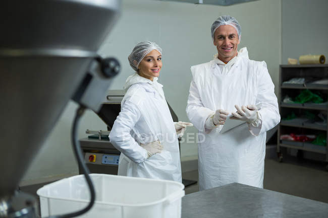 Carniceros masculinos y femeninos de pie con informe y sonriendo en la fábrica de carne - foto de stock