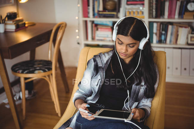 Mulher ouvindo música com fones de ouvido e tablet digital na sala de estar em casa — Fotografia de Stock