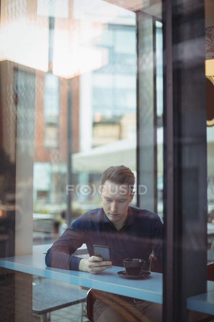 Мужчина, использующий мобильный телефон у стойки в столовой — стоковое фото