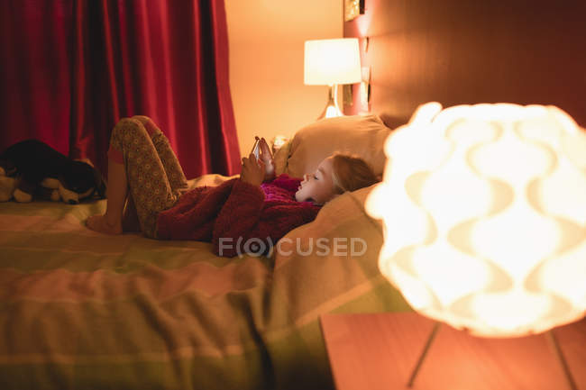 Девочка использует цифровой планшет, расслабляясь на кровати дома — стоковое фото