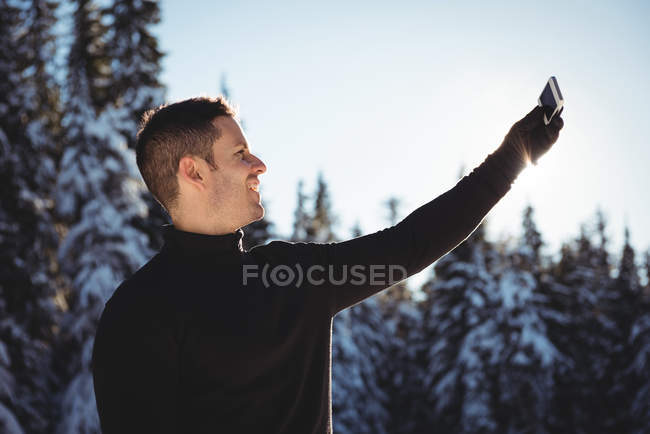 Homme souriant prenant selfie sur téléphone portable pendant l'hiver — Photo de stock