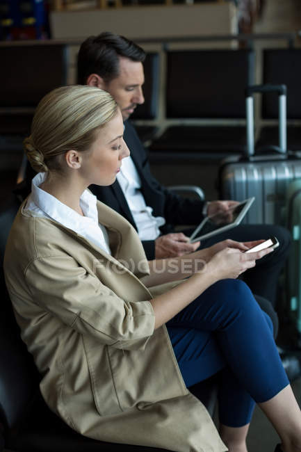 Sección media de la pareja usando teléfono móvil y tableta digital en el aeropuerto - foto de stock