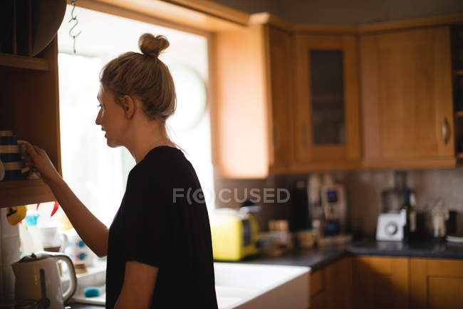 Frau holt Kaffeetasse zu Hause aus Küchenschrank — Stockfoto