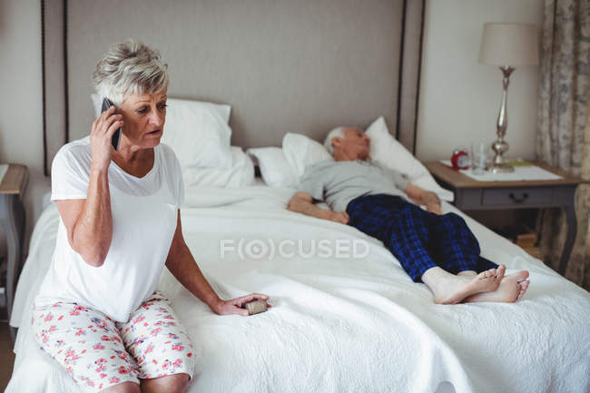 Занепокоєна старша жінка сидить у спальні, тримає ліки і розмовляє на мобільному телефоні — стокове фото