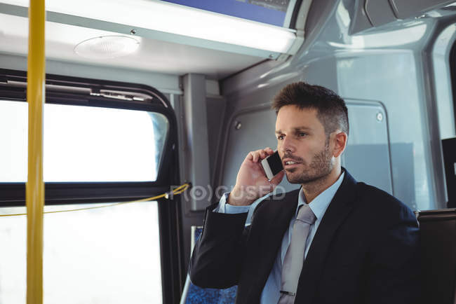 Бизнесмен разговаривает по мобильному телефону во время поездки в автобусе — стоковое фото