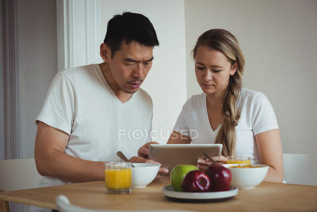 Couple using digital tablet while having breakfast at home — Stock Photo