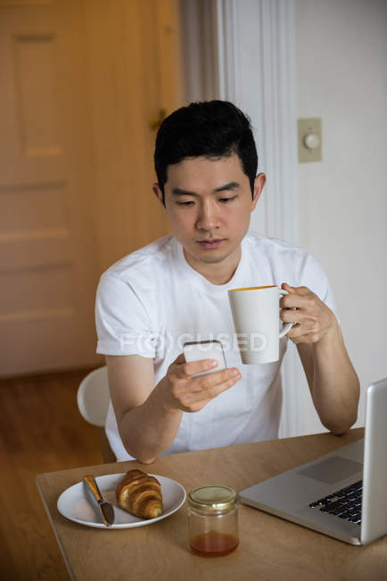 Чоловік використовує мобільний телефон, маючи чашку кави вдома — стокове фото