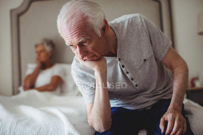Беспокойный старший мужчина сидит с рукой на подбородке в спальне — стоковое фото