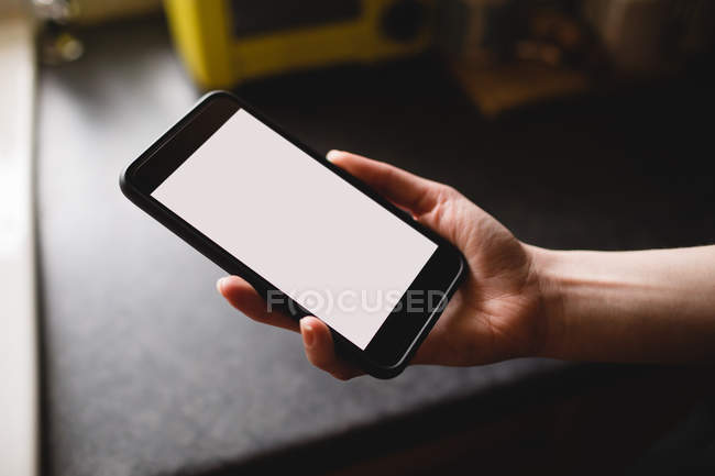 Womans hand holding mobile phone in the kitchen at home — Stock Photo