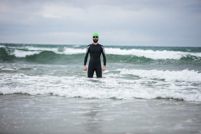 Athlète en combinaison humide debout dans la mer sur la plage — Photo de stock
