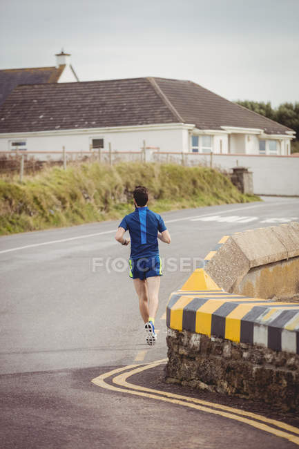 Вид сзади на человека, совершающего пробежку по открытой дороге — стоковое фото