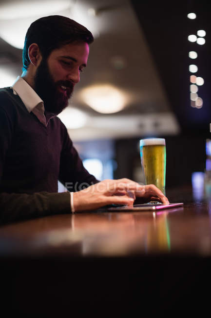 Mann benutzt digitales Tablet mit Bierglas auf Theke in Bar — Stockfoto