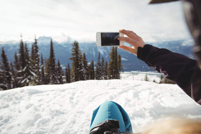 Abgeschnittenes Bild einer Person, die am schneebedeckten Berg gegen Bäume fotografiert — Stockfoto
