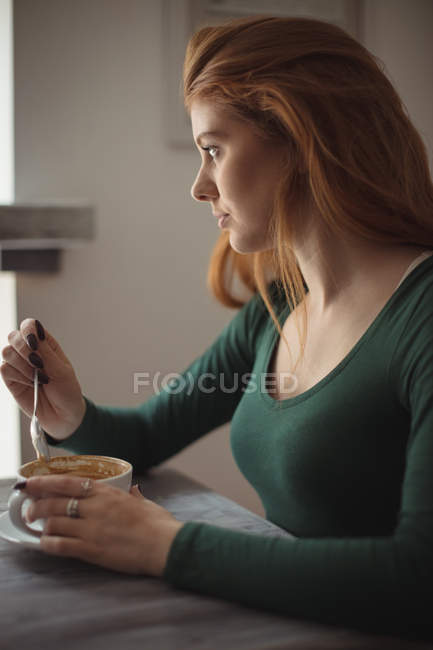 Mujer joven revolviendo café en la taza en el restaurante - foto de stock