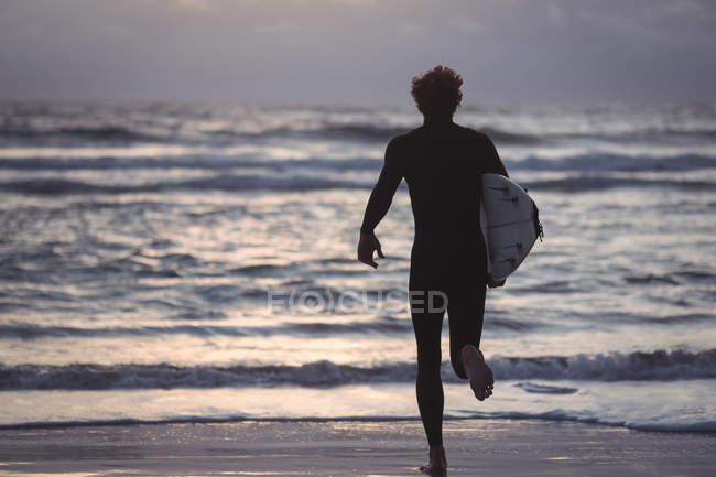 Silhouette di un uomo che porta la tavola da surf che corre verso il mare al crepuscolo — Foto stock