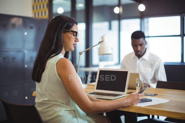 Businesswoman using mobile phone at her desk in office — Stock Photo