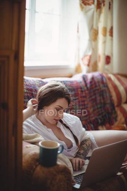 Bella donna sdraiata sul divano e utilizzando il computer portatile in soggiorno a casa — Foto stock