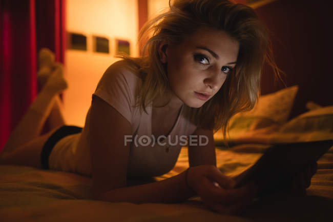 Femme couchée et utilisant une tablette numérique sur le lit dans la chambre — Photo de stock