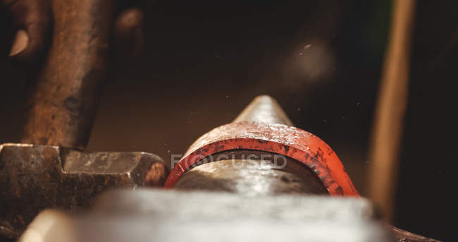 Крупный план кузнеца, держащего красную металлическую подкову с щипцами на наковальне с помощью молотка в форме — стоковое фото