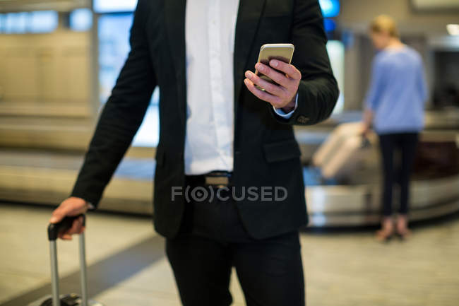 Mid section of businessman using mobile phone in waiting area at airport terminal — Stock Photo
