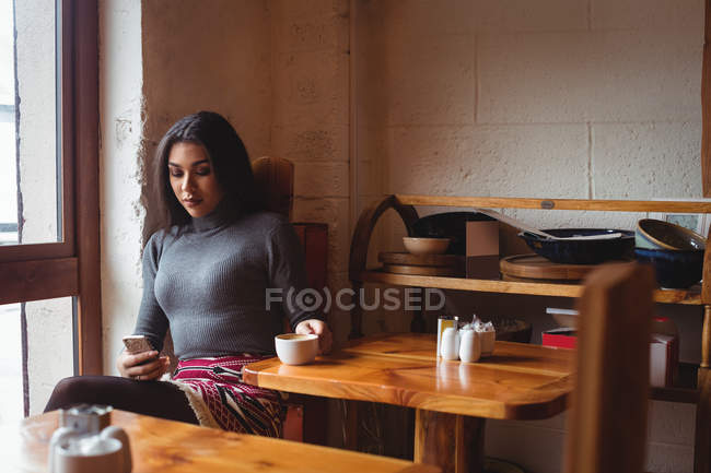 Bella donna che utilizza il telefono cellulare mentre si beve una tazza di caffè al caffè ?? — Foto stock