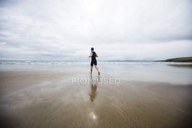 Vue arrière de l'homme en maillot de bain et bonnet de bain courant sur la plage — Photo de stock