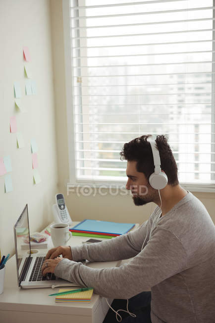 Vista lateral del hombre usando el ordenador portátil mientras está sentado en el escritorio - foto de stock