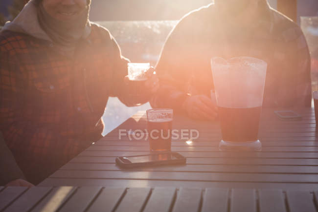 Amici maschi che hanno occhiali di birra in stazione sciistica su una luce del sole lucente — Foto stock