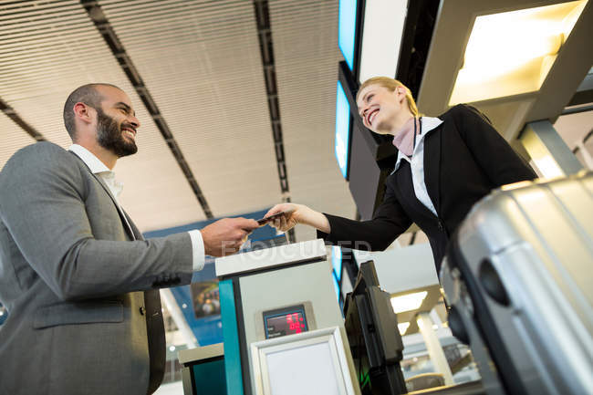 Atendedor de check-in da companhia aérea entrega cartão de embarque para pendulares no balcão no terminal do aeroporto — Fotografia de Stock