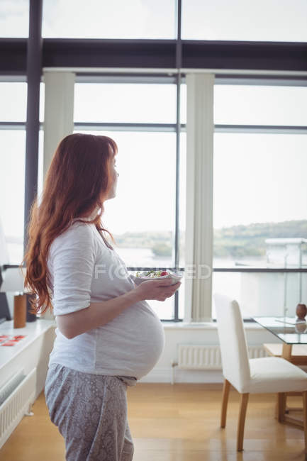 Thoughtful pregnant woman holding bowl of salad at home — Stock Photo