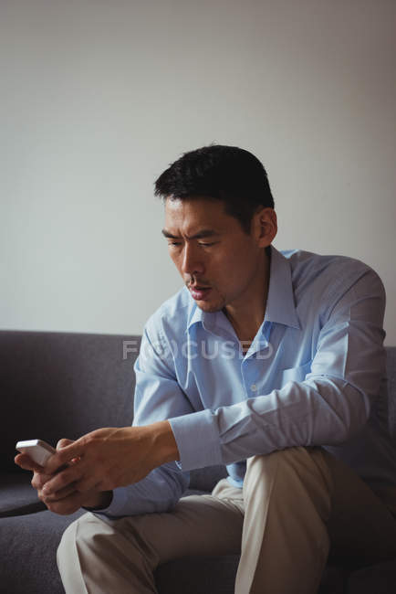 Homme utilisant un téléphone portable dans le salon à la maison — Photo de stock