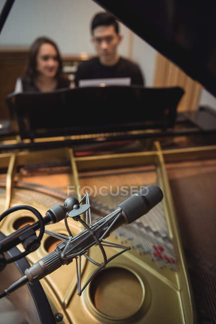 Крупним планом мікрофон у студії звукозапису з людьми на піаніно у фоновому режимі — стокове фото