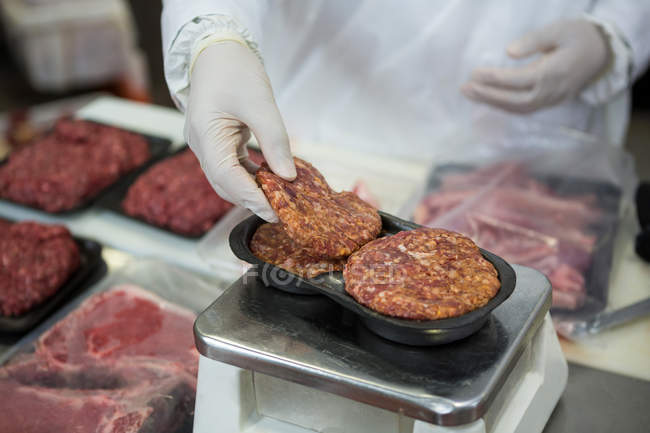 Primer plano del carnicero que pesa empanadas de carne a escala en la fábrica de carne - foto de stock