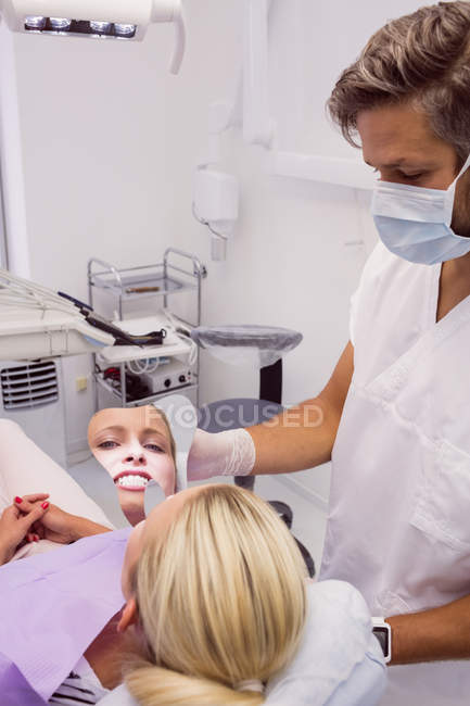 Dentista sosteniendo espejo cerca de la cara del paciente en la clínica - foto de stock