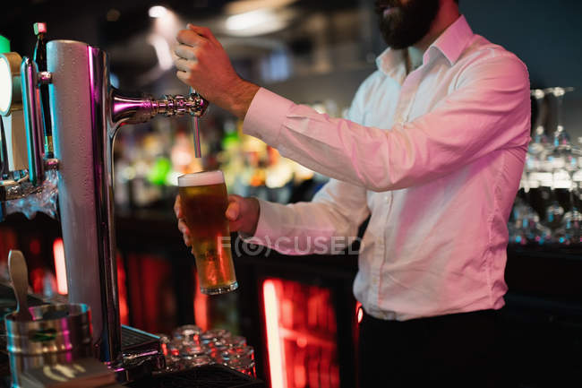 Sección media del camarero llenando cerveza de la bomba de bar en el mostrador de bar - foto de stock