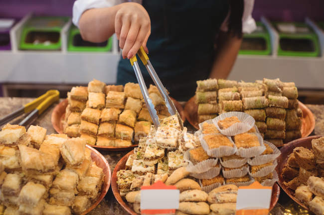 Средняя секция продавщицы, занимающаяся организацией турецких сладостей у прилавка в магазине — стоковое фото