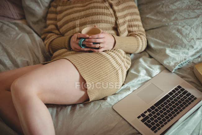 Sección media de la mujer acostada en la cama con el ordenador portátil en casa - foto de stock