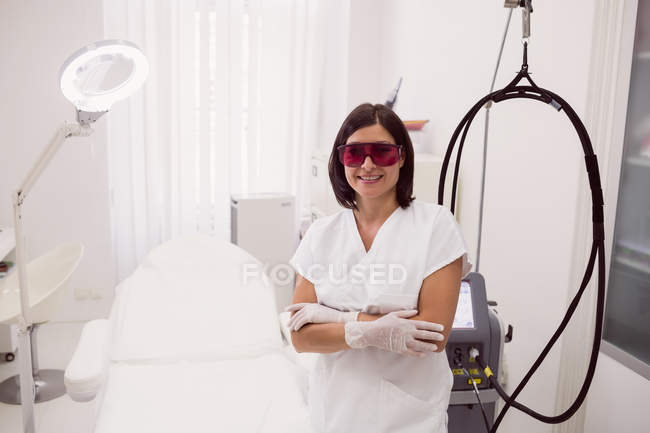 Лікар в захисних окулярах, що стоять з обіймами, схрещеними в клініці — стокове фото