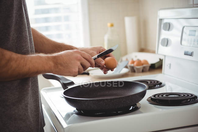 A meio da secção do homem a partir um ovo numa frigideira na cozinha em casa — Fotografia de Stock