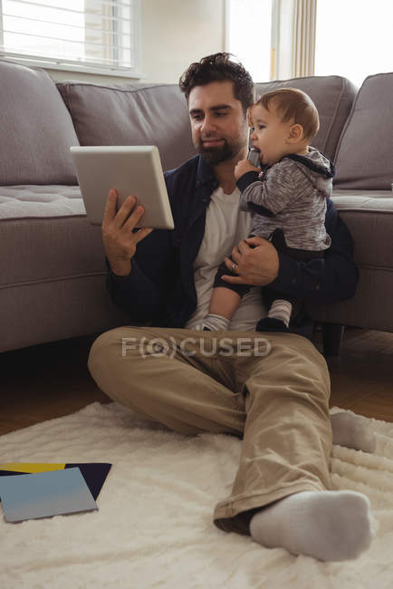 Отец держит своего ребенка во время использования цифрового планшета дома — стоковое фото