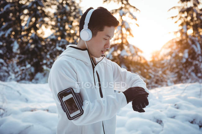 Hombre asiático ajustando tiempo en smartwatch durante el invierno - foto de stock