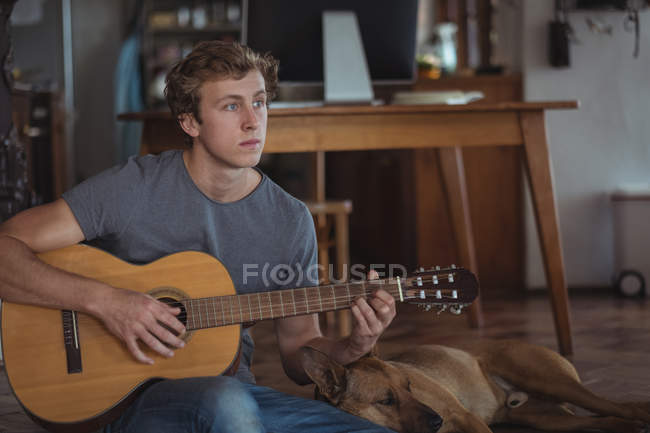 Man playing guitar at home, dog lying beside him — Stock Photo