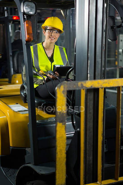 Retrato de trabajadora con tablet digital en carretilla elevadora en almacén - foto de stock
