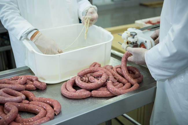 Sezione intermedia dei macellai che lavorano salsicce in fabbrica di carne — Foto stock