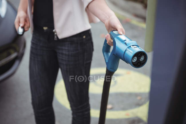 Средняя часть женщины заряжает электромобиль на улице — стоковое фото