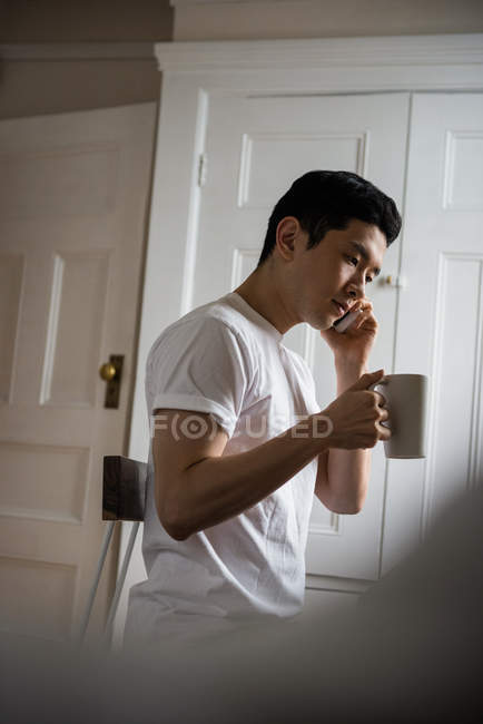 Чоловік розмовляє на мобільному телефоні, маючи чашку кави вдома — стокове фото